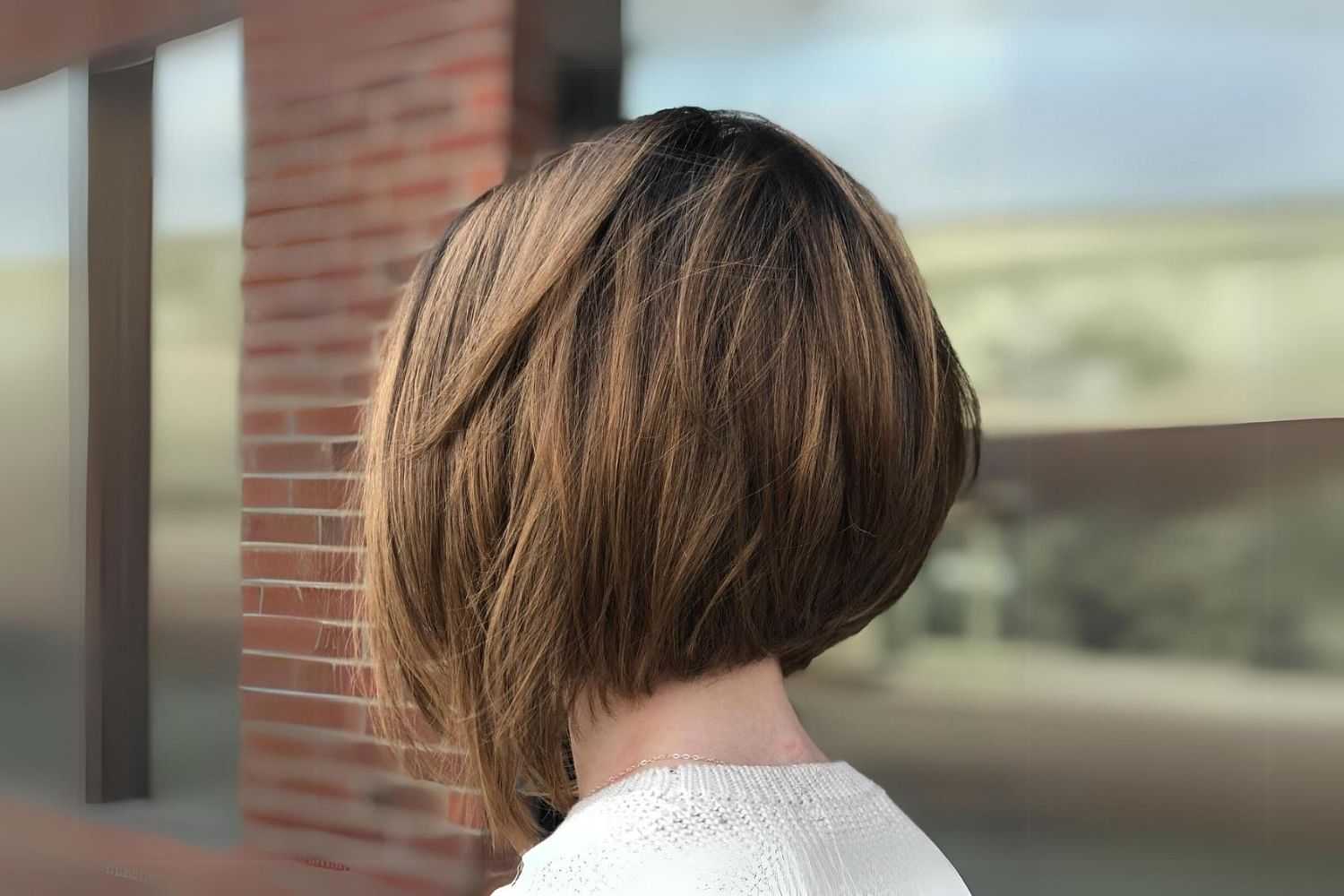 Back view of a person with a short, layered bob haircut, standing near a brick wall.