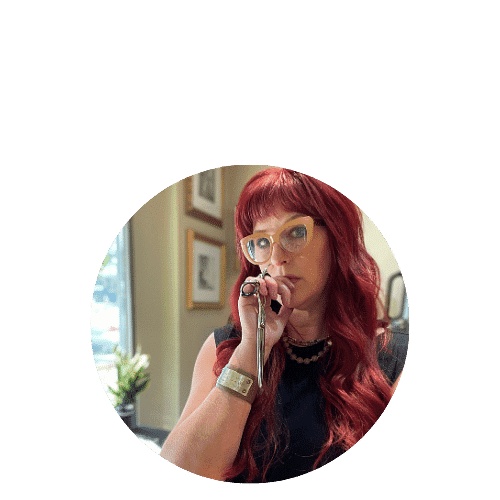 Woman with red hair and glasses, holding a microphone in a modern room with framed pictures.